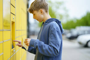 Junge mit Fahrkarte gibt Daten in den Paketautomaten ein - NJAF00367