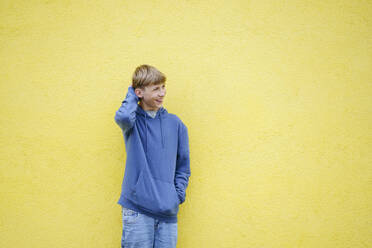 Glücklicher blonder Junge vor gelber Wand stehend - NJAF00370