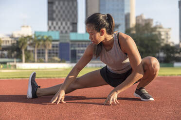 Junge Frau macht Beintraining auf einem Sportplatz - IKF00850