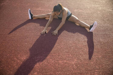 Young woman doing stretching exercise in sports field - IKF00852