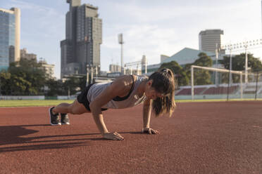 Young woman practicing push ups at sports field - IKF00853