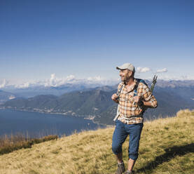 Lächelnder Mann, der an einem sonnigen Tag auf einem Berg spazieren geht - UUF28889