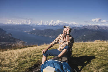 Glücklicher Wanderer auf einer Bank sitzend an einem sonnigen Tag - UUF28909