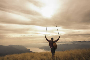 Woman holding hiking poles in hands looking at sunset - UUF28923