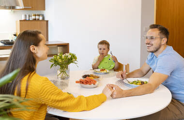 Boy looking at smiling parents holding hands at dining table - NDEF00740