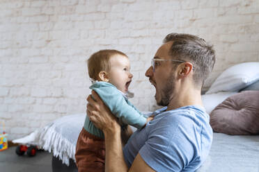 Playful father screaming with baby boy at home - NDEF00746