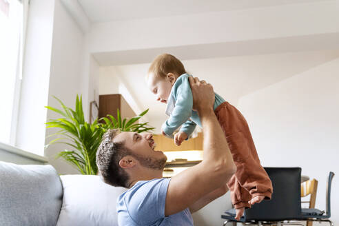 Father lifting cute baby boy in living room at home - NDEF00747