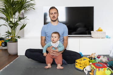 Vater meditiert sitzend mit kleinem Jungen im Wohnzimmer zu Hause - NDEF00749