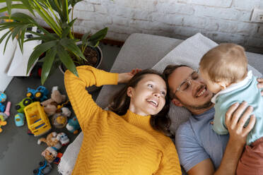 Glückliche Eltern verbringen ihre Freizeit mit einem kleinen Jungen, der zu Hause auf der Couch liegt - NDEF00760