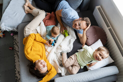 Parents spending leisure time with children playing on couch at home - NDEF00762