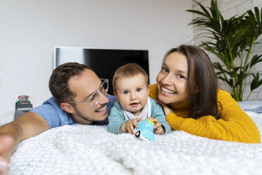 Niedlicher kleiner Junge mit Eltern auf der Couch liegend zu Hause - NDEF00763