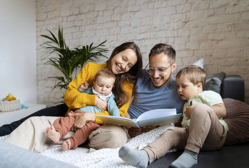 Glückliche Eltern lesen ein Buch für ihre Kinder auf der Couch zu Hause - NDEF00764