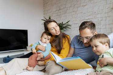 Parents reading book for children on couch at home - NDEF00765