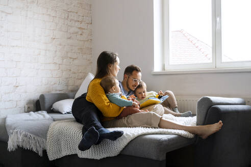 Eltern lesen mit ihren Kindern auf der Couch zu Hause ein Buch - NDEF00766