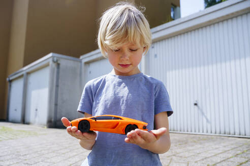 Boy holding toy car in yard outside garage - NJAF00380