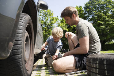 Vater und Sohn wechseln Autoreifen im Hof - NJAF00383