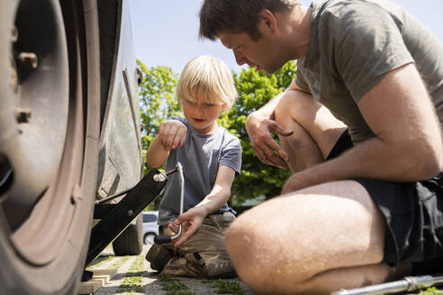 Father and son changing car tire in yard - NJAF00384