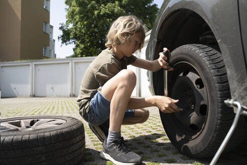 Junge wechselt Autoreifen im Hof - NJAF00387