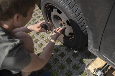 Boy repairing car tire in yard - NJAF00390