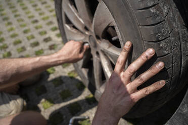 Hände eines Mannes, der einen Autoreifen im Hof wechselt - NJAF00394