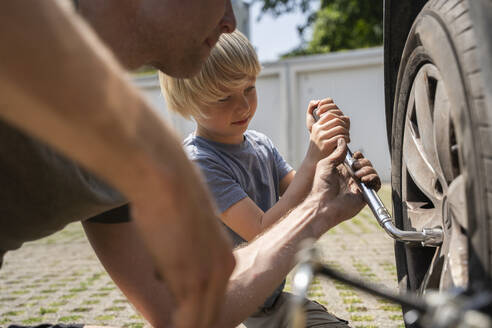 Man changing car tire with son in yard - NJAF00396