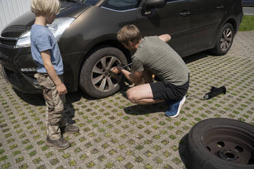 Junge beobachtet Vater bei der Reparatur von Autoreifen im Hof - NJAF00398