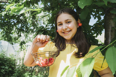 Playful girl holding cherry basket in garden - OSF01724
