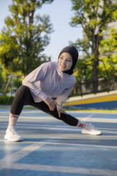 Lächelnde Frau beim Stretching auf dem Sportplatz - IKF00867