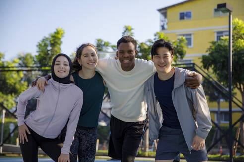 Lächelnder Mann, der seine Freunde auf dem Sportplatz umarmt - IKF00883