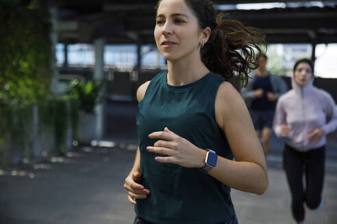 Woman wearing smart watch jogging with friends - IKF00896