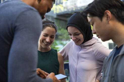 Happy friends looking at smart phone held by man - IKF00899