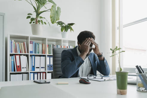 Geschäftsmann mit Kopf in der Hand am Schreibtisch im Büro - OSF01731