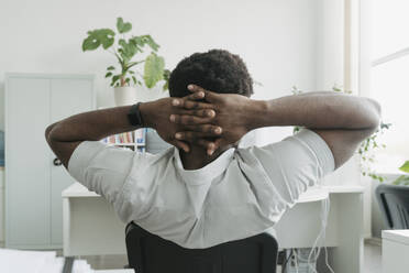 Businessman resting with hands behind head at office desk - OSF01746