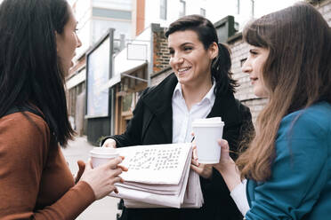 Lächelnde Geschäftsfrau mit Zeitung in der Hand und Gespräch mit Bürokollegen - AMWF01405