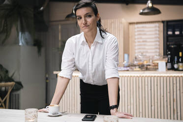 Confident businesswoman leaning on table at cafe - AMWF01425