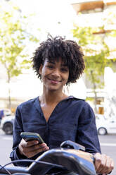 Lächelnde Frau mit Smartphone und Elektrofahrrad - PNAF05347