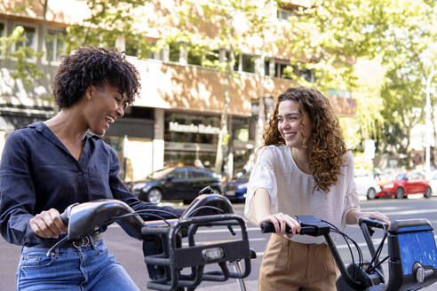 Glückliche Freunde mit Elektrofahrrad an einer Parkstation - PNAF05348