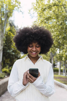 Lächelnde Afro-Frau mit Smartphone im Park - PNAF05401