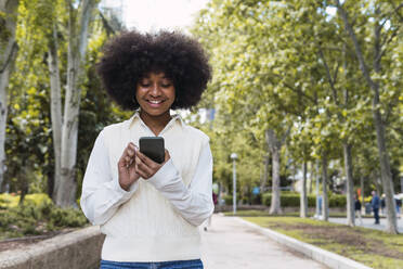 Glückliche Afro-Frau mit Smartphone im Park - PNAF05403