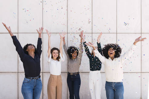 Happy businesswomen together celebrating with confetti in front of wall - PNAF05416