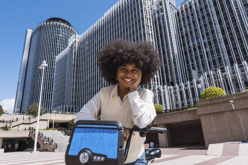 Glückliche junge Geschäftsfrau mit Elektrofahrrad im Büropark stehend - PNAF05434