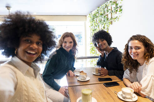 Eine Gruppe fröhlicher Freunde posiert für ein Selfie mit einer glücklichen jungen Frau in einem gemütlichen Café - PNAF05448