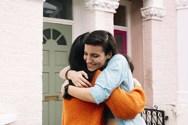 Lächelnde Freunde umarmen sich vor dem Haus - AMWF01427