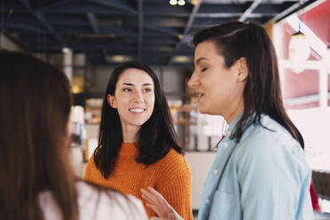 Smiling friends discussing at cafe - AMWF01433