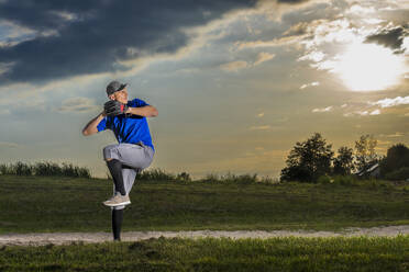 Junger Mann spielt Baseball auf Gras in der Dämmerung - STSF03732