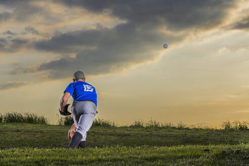 Mann wirft Baseball im Gras stehend in der Abenddämmerung - STSF03733