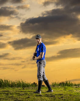 Junger Mann hält Baseballschläger mit Himmel im Hintergrund in der Abenddämmerung - STSF03734