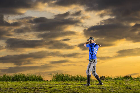 Junger Baseballspieler, der in der Abenddämmerung auf dem Rasen stehend eine Aufnahme macht - STSF03735