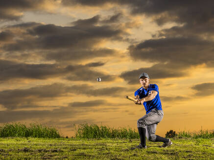 Mann in Sportkleidung, der in der Dämmerung einen Baseball mit einem Schläger schlägt - STSF03736