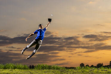Young man jumping and catching baseball at dusk - STSF03741